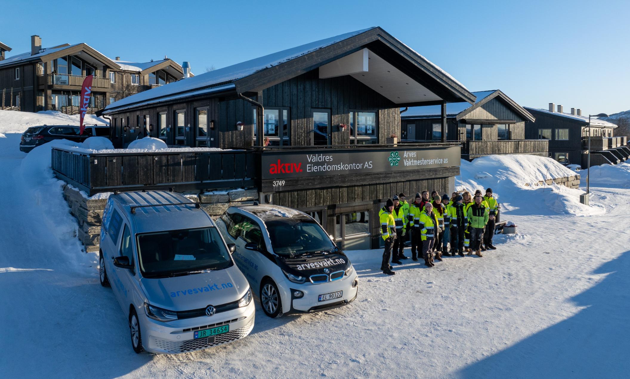 Arbeidsbiler og mennesker foran hus